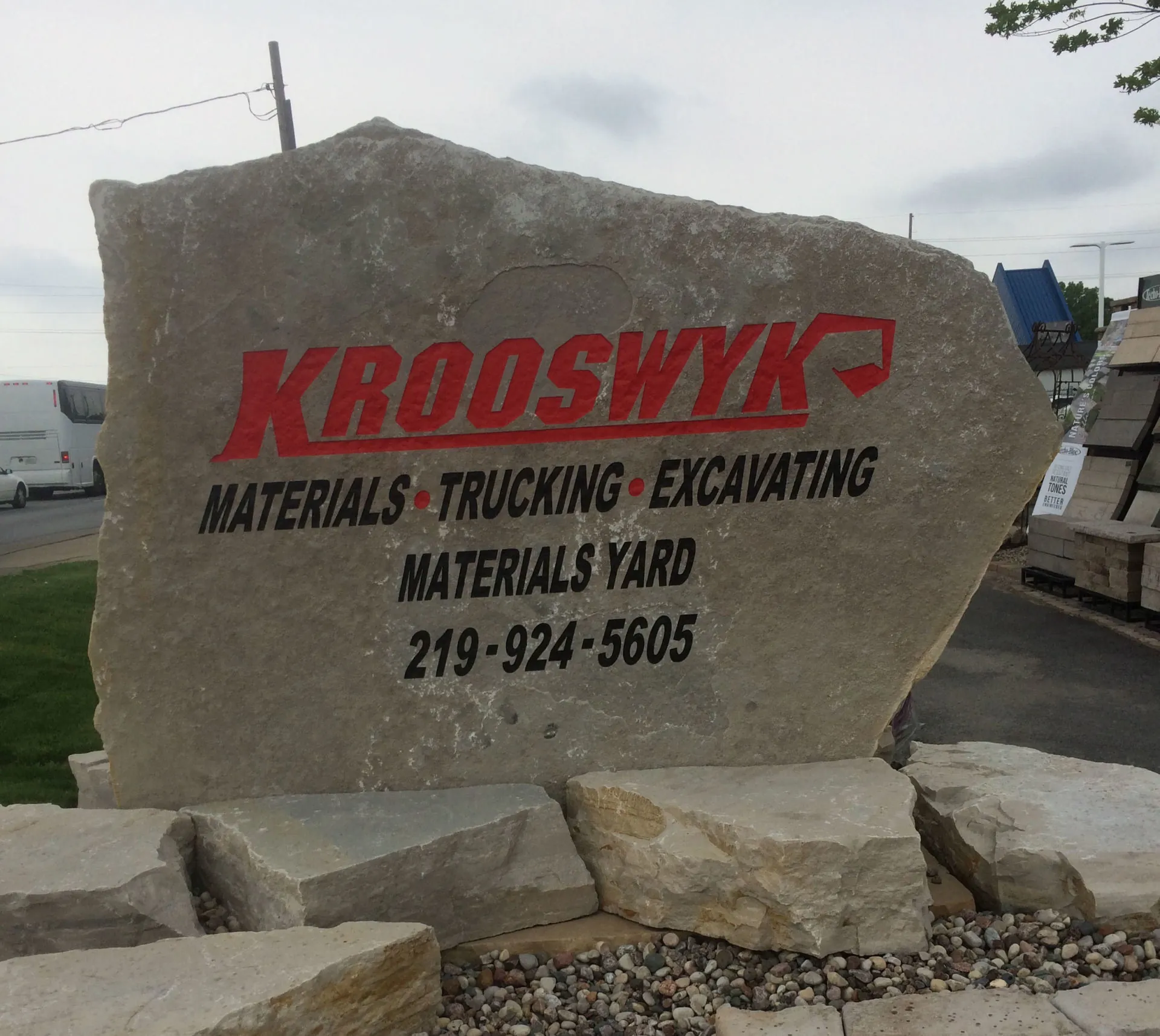 The Krooswyk Materials Yard boulder sign at the yard entrance, with stone and paver displays behind it