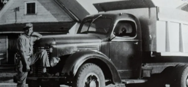 Historic black-and-white photo of a man beside a vintage Krooswyk dump truck