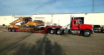 A red Krooswyk semi hauling an excavator on a lowboy trailer